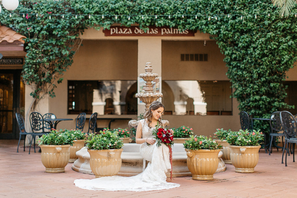 bride sitting on fountain in courtyard at mission inn wedding with florals