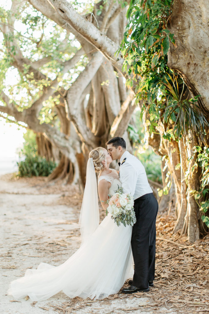 bride and groom kissing under the banyan trees gasparilla island boca bay pass club wedding
